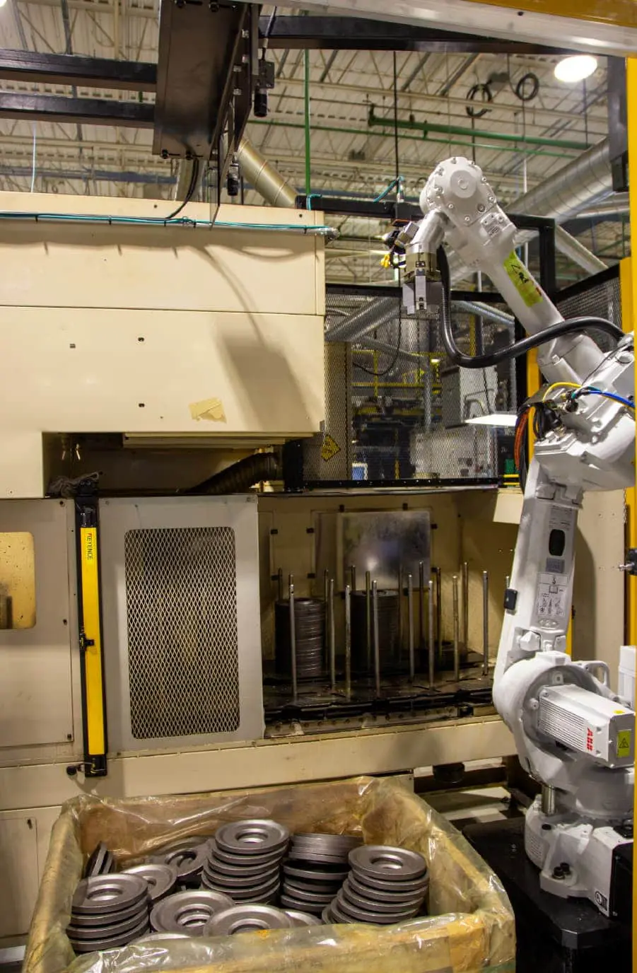 This is the complete cell design, with the ABB industrial robot with a custom end-of-arm tool, the deep plastic-lined bin filled with parts, and the two 2D cameras used by Apera AI for scene acquisition positioned overhead. The robot picks the unmachined discs and stacks them in the middle of the picture.